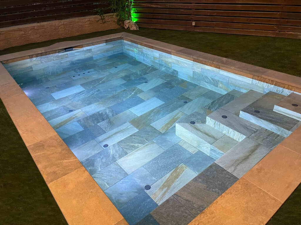 piscina de obra en olius, vista de noche con iluminación led, donde se aprecia el sistema integrado de limpieza automático, las escaleras y el banco.